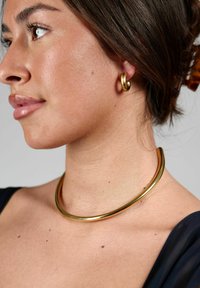 Guldfarvet metal smykke med en glat, rund choker og en matchende hoops-ørering, der fremhæver en poleret, reflekterende finish.