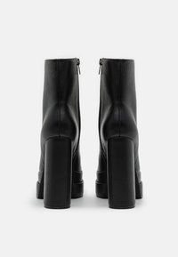 Black leather ankle boots with a smooth finish, high block heels, and zip closures at the back. Featuring a sleek, modern design.