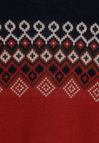 Pletený svetr s tmavě modrým a červeným geometrickým vzorem, se bílými a zelenými akcenty; hladká textura a kulatý výstřih.
