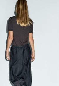 Bruine top met korte mouwen, gecombineerd met donker, loszittende, elastische taillebroeken; gladde stof met een subtiele textuur, gezien van achteren.