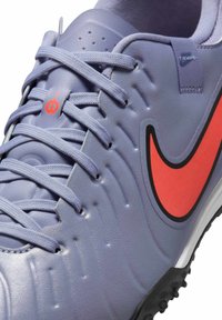 Purple synthetic soccer shoe featuring textured upper, red Nike swoosh, and gray rubber outsole with studs. Includes gray laces.