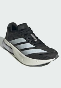 Zwarte sportieve schoen met een bovenwerk van mesh, voorzien van drie witte strepen, een gevoerde zool en opvallende branding op de tong en zijkant.