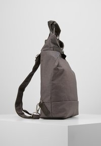 Bolso de hombro de tela gris con un diseño elegante, que cuenta con una base plana, correa ajustable y acentos de hardware metálico.