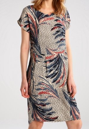 Femme portant une robe beige mi-longue à manches courtes avec des motifs abstraits de feuilles bleu, rouge et noir.