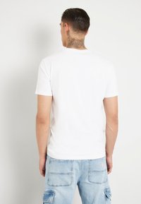 T-shirt blanc à manches courtes avec col rond, fabriqué en coton doux, associé à un jean cargo bleu clair avec de nombreuses poches.