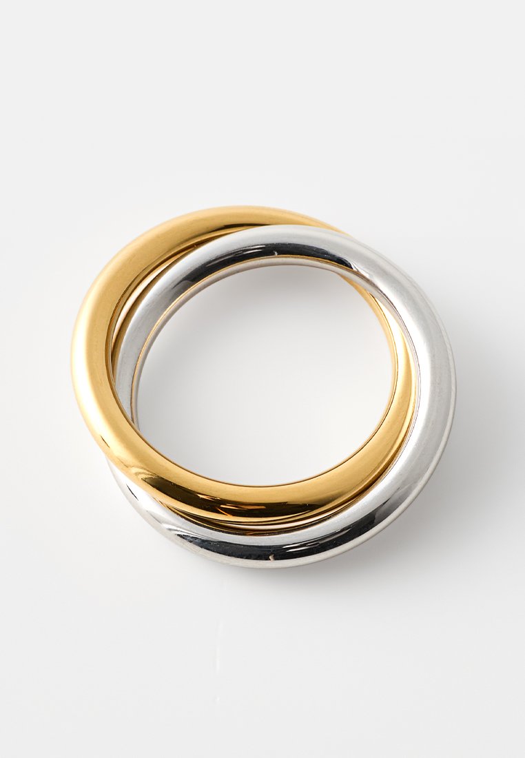 Deux anneaux imbriqués—un en ton or et un en ton argent—tous deux avec une finition polie, des surfaces lisses et des formes arrondies.