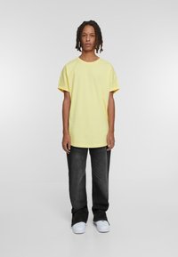Camiseta de algodón amarilla con corte relajado y mangas enrolladas, combinación con jeans gris oscuro y zapatillas blancas. Diseño simple, sin patrones.