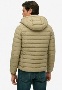 Giacca puffer beige con strisce orizzontali, cappuccio e design attillato, abbinata a jeans blu scuro. Texture liscia, aspetto leggero.