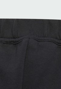 Pantalons de survêtement en coton noir avec une texture douce, une taille élastique et des coutures décoratives le long des seams. Idéaux pour une tenue décontractée.
