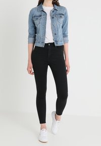 Svetle modrá džínová bunda, přiléhavé bílé tričko, černé skinny džíny a bílé tenisky. Výrazné prošívání na bundě a štíhlý silueta.