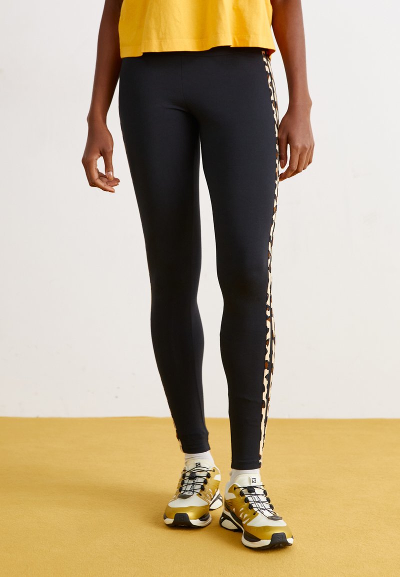 Fekete leggings, oldalt leopárdmintás csíkkal, arany és fekete sportcipővel párosítva. A felső egy rövidített sárga póló.