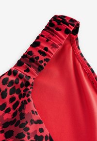 Gros plan sur un tissu de maillot de bain rouge à imprimé léopard noir avec des détails froncés sur la bretelle.