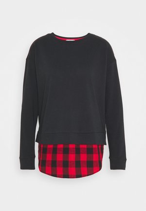 Sort langærmet crewneck sweatshirt lagdelt over en rød og sort ternet skjorte med synlig nederste kant.