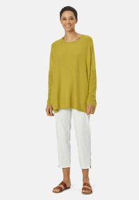 Pull oversized vert lime avec des manches longues et des accents côtelés. Associé à un pantalon blanc cropped avec des zips au bas et des sandales marron.