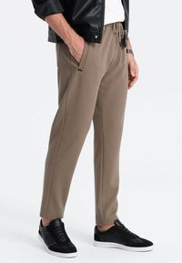 Bruine trainingsbroek van een textuurstof, met een trekkoord in de taille en zijzakken, gecombineerd met zwarte sneakers.
