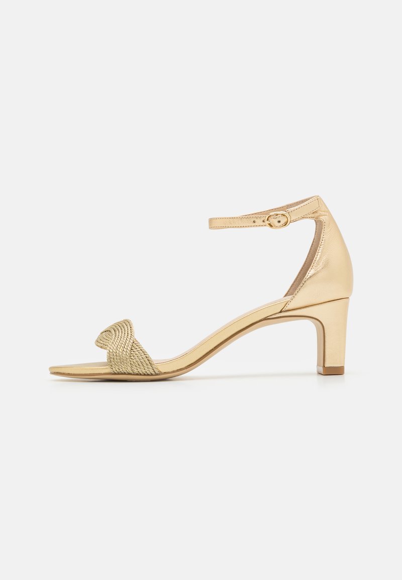 Gold heeled sandal with a woven strap across the toe and an ankle strap. Features a geometric design and a polished finish. Mid-height heel.