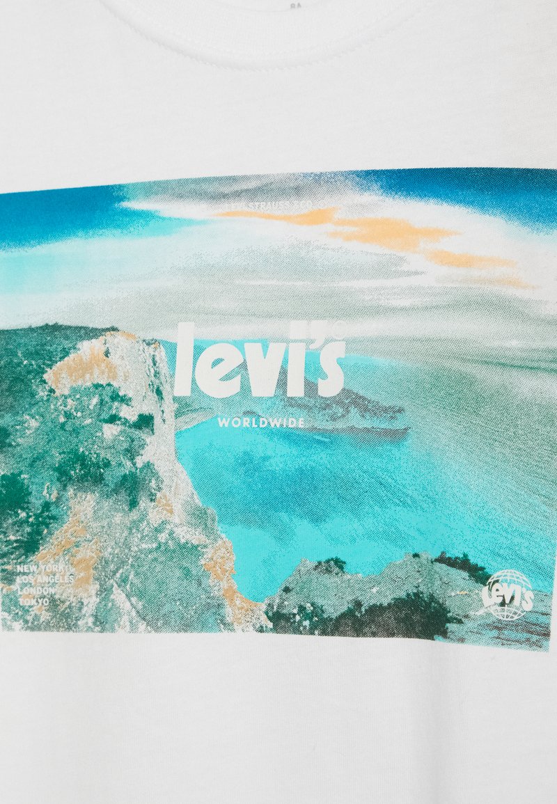 Biała bawełniana koszulka z kolorowym nadrukiem przedstawiającym nadmorski krajobraz. Tekst zawiera słowa "Levi's" i "Worldwide" w wyraźnych literach.
