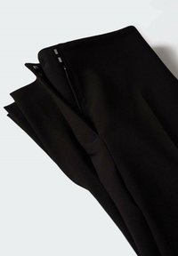 Pantalon noir au design ajusté, confectionné dans un tissu lisse. Les détails notables incluent une fermeture éclair cachée et des lignes nettes et droites.