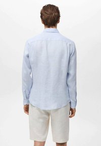 Camisa de manga larga azul clara de lino, con cuello clásico y puños abotonados, combinada con pantalones cortos beige.