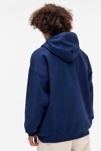 Felpa blu navy con cappuccio, spalle scese e polsini a coste, caratterizzata da una texture morbida e una vestibilità rilassata, vista da dietro.
