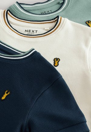 Drei Pullover in Marineblau, Weiß und Hellgrün. Jeder hat einen gerippten Kragen und ein besticktes Hummerdesign. Strukturierter Stoff.