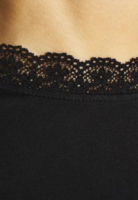 Svart topp med en delikat blommig spetsdetalj vid halslinningen, tillverkad av mjukt, slätt material med figursydd passform.