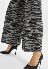 Vrouw in een ruime zebra-print broek en zwarte puntige hoge hakken op een effen witte achtergrond.