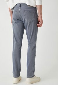 Jeans de mezclilla gris claro con corte slim, que presentan dos bolsillos en la parte trasera y detalles de costura sutiles, combinados con zapatillas blancas.