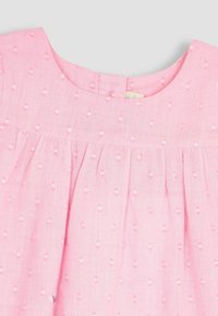 Vestido rosa claro con una superficie texturada que presenta puntos en relieve. Escote redondo y detalle de tela fruncida en el cuerpo. Cierre en la parte posterior con botones.