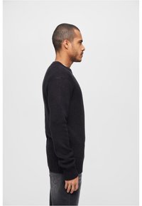 Jersey negro de punto con mangas largas, puños acanalados y cuello redondo; diseño texturizado, de grosor medio y ajustado, mostrado de lado.