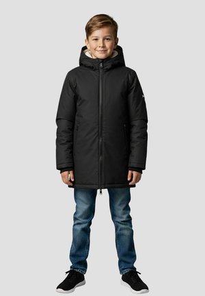 Zwarte geïsoleerde parka met capuchon en ritssluiting aan de voorkant. Voorzien van zijzakken, een zachte voering aan de binnenkant en lange mouwen; gecombineerd met een blauwe spijkerbroek en zwarte schoenen.
