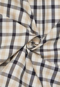 Tessuto di cotone con un motivo a quadri che presenta quadrati alternati in beige, crema e nero, mostrando diverse texture e profondità.
