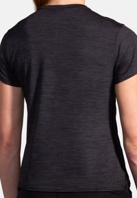 Camiseta deportiva de manga corta, negra, con un tejido texturizado, diseño ajustado y dobladillo curvado. Sin logotipos ni acentos visibles.