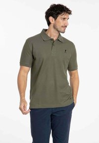Polo de couleur vert olive en coton, avec un col, des manches courtes et un petit logo noir brodé sur le côté gauche de la poitrine.
