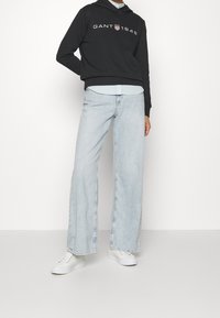 Czarna bluza z nadrukiem z przodu, nałożona na jasnoniebieską, paskowaną koszulę. W komplecie z jasnoniebieskimi, szerokimi spodniami dżinsowymi i białymi trampkami.