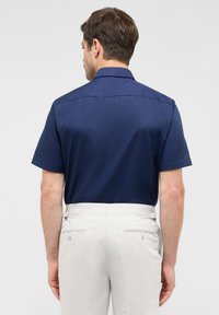 Korte mouw donkerblauwe shirt met een kraag, een gladde textuur en een getailleerde pasvorm, gecombineerd met lichtgekleurde broeken met achterzakken.
