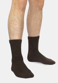 Braune gerippte Socken mit weicher Textur, mit umgeschlagenem Bund und nahtloser Zehenpartie, an nackten Unterschenkeln gezeigt.