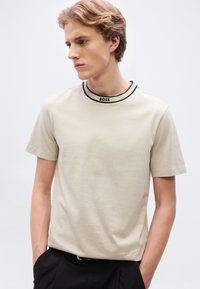 Μπεζ T-shirt με κοντά μανίκια, μαύρο ριμπ κορδόνι με το λογότυπο "BOSS", κατασκευασμένο από απαλό βαμβακερό ύφασμα. Απλός και κλασικός σχεδιασμός.