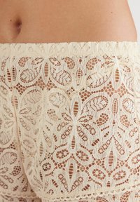 Kanten shorts met bloemmotief, voorzien van ingewikkelde uitsparingen en een zachte crème kleur. Elastische tailleband en gedetailleerde kanttextuur.