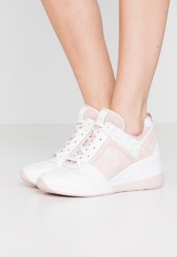 Witte en lichtroze sneakers met een textuur bovenwerk, gestreepte accenten en een wigzool; vetersluiting en gewatteerde kraag.