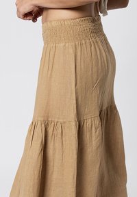 Beige gelaagde maxi rok van lichtgewicht stof, met een gesmokte hoge tailleband en gathering naden voor extra textuur.