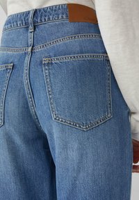 Hellblaue Jeans mit hoher Taille, ausgestattet mit zwei Gesäßtaschen und einem braunen Lederlabel am Bund. Sauberes, klassisches Design.