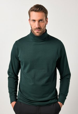 Donkergroen coltrui gemaakt van een gladde stof, met lange mouwen en een aansluitend ontwerp, gedragen met handen in de zakken.