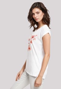 White cotton T-shirt featuring a floral design in pink tones, short rolled sleeves, loose fit, and rounded hem.
