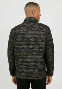 Veste rembourrée camouflage de couleur vert foncé et noir avec un matelassage horizontal. Elle possède un col montant et des manches longues.