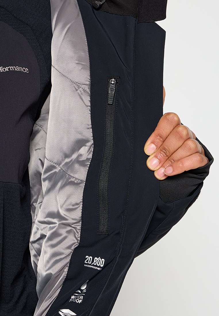 Hand die een open zwarte waterdichte jas vasthoudt, waarbij de binnenzak met rits en de zilveren gewatteerde voering zichtbaar zijn, samen met het etiket voor waterdichte beoordeling.