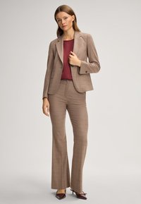 Beige kariertes Blazer mit passender Hose, kombiniert mit einem burgunderfarbenen Oberteil. Hat ein tailliertes Design und eine glatte Stofftextur. Hochhackige Schuhe in tiefem Burgunder.