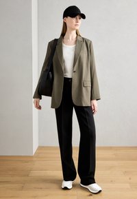 Olive zielony, oversize'owy żakiet, biały t-shirt, czarne dopasowane spodnie, czapka w kolorze czarnym oraz białe sneakersy, z czarną torebką na ramię. Minimalistyczny design.