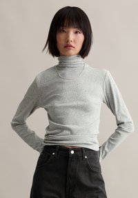 Lichtgrijze langslijf turtleneck van zacht, geribbeld stof met een strakke pasvorm. Gecombineerd met hoge zwarte denim. Zilveren ketting.