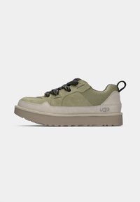 Oliva zöld velúr és hálós felsőrészű sneaker, fekete cipőfűzővel és bézs talppal. Jellemzője a mintázott dizájn és a hátsó húzószalag. Az UGG logó látható.